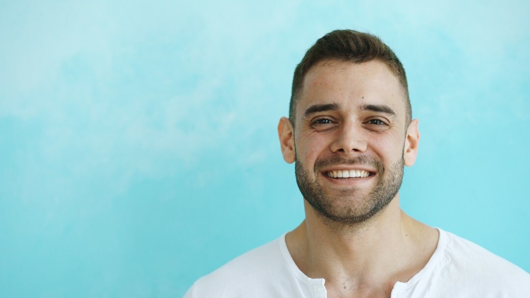 Studio portrait of a smiling Hispanic man with short hair against a blue background